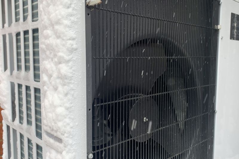 Showing the outdoor unit for an air source heat pump operating in the snow